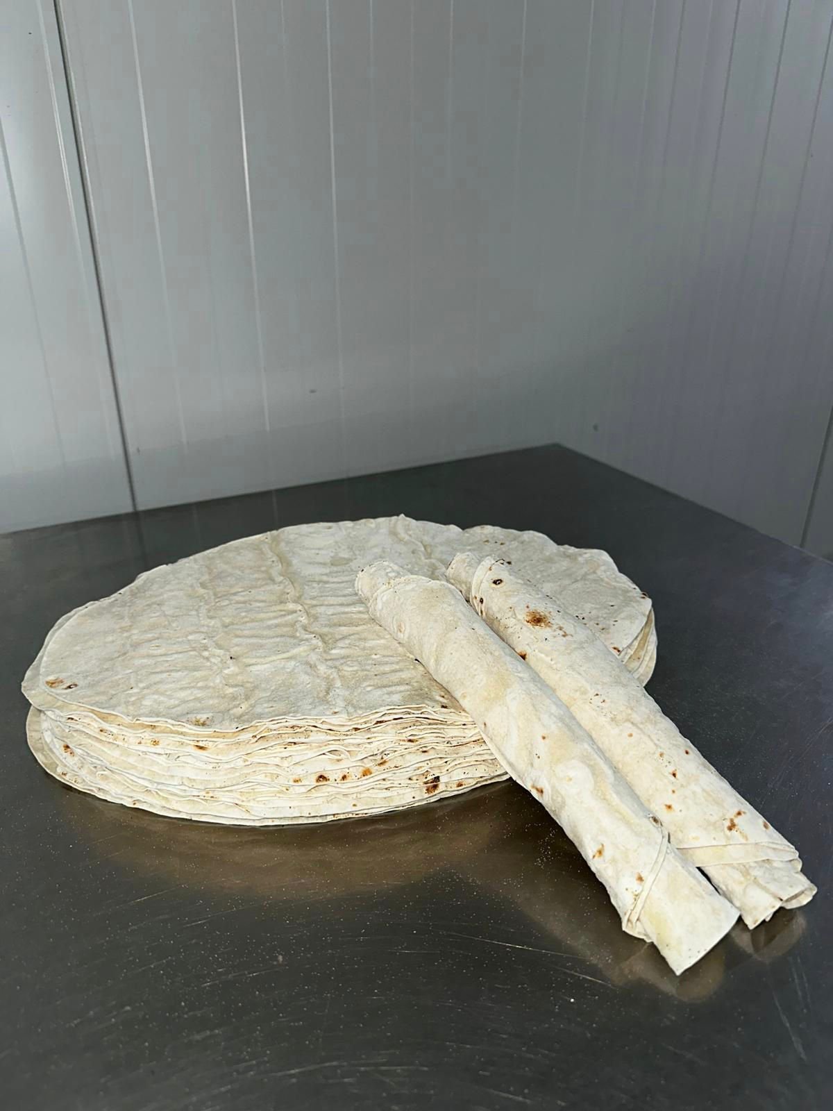 Three rolled Dürüm Lavaş on dark wood with spilled flour